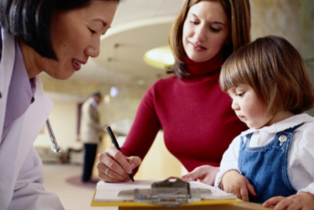 Mother and child signing papers while doctor looks over